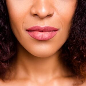 Close-up of a woman with dark skin wearing a matte mauve pink lipstick.