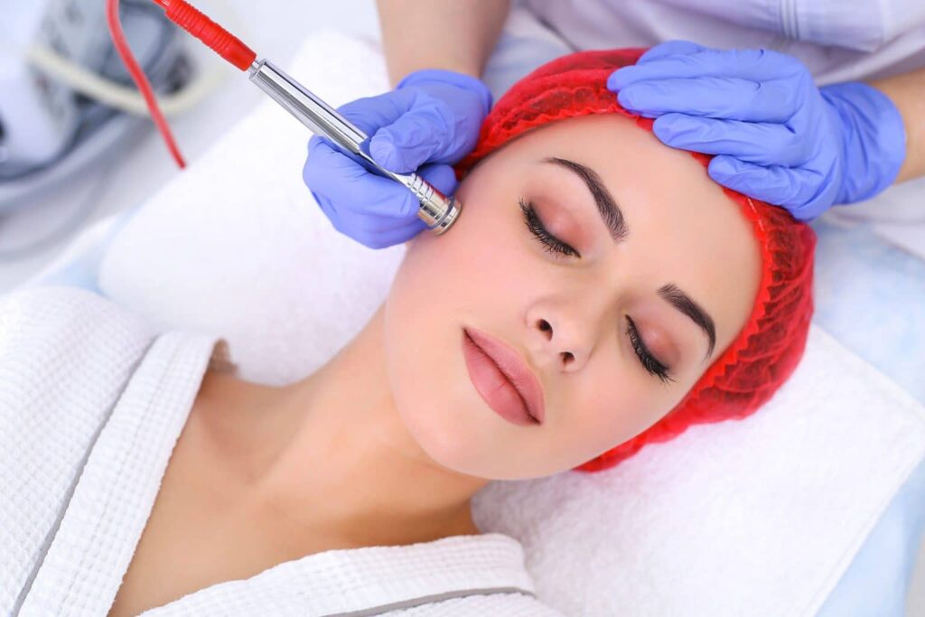 A woman receiving a professional microdermabrasion facial treatment from an aesthetician wearing blue gloves.