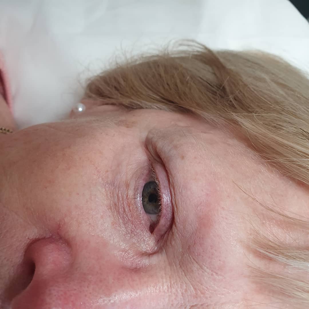 A close-up, slightly angled view of a person's right eye, showing the iris, lashes, and surrounding skin with blonde hair.